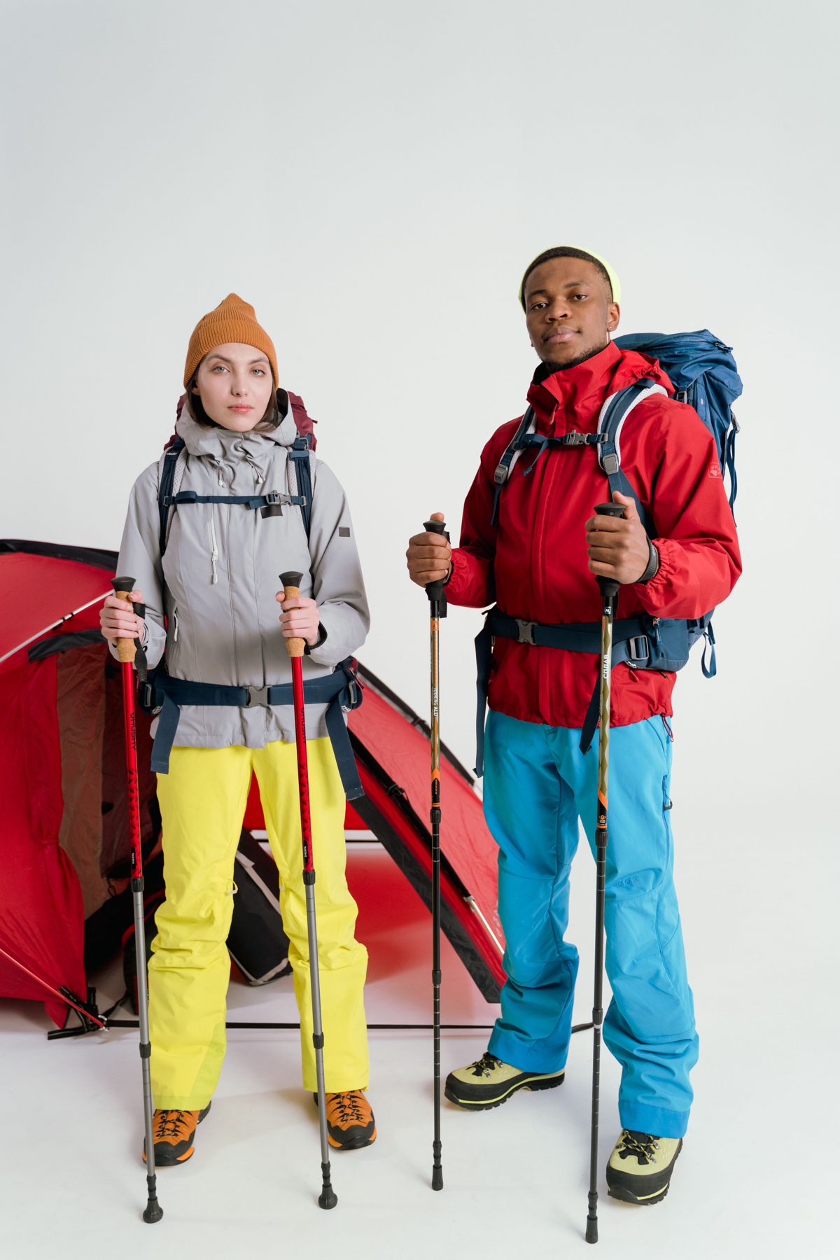 Hikers with backpacks and trekking poles ready for a camping trip beside a red tent